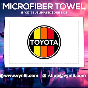 May include: White microfiber towel, 45.7cm x 30.5cm, featuring a Toyota logo. The logo is a circle with yellow, orange, and red vertical stripes and the word "TOYOTA" in black. The towel is sublimated on one side.