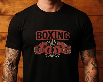 May include: A black short-sleeved t-shirt featuring a graphic print on the chest. The design includes the word BOXING in red capital letters above two red boxing gloves facing each other, accented with white radiating lines and cross-lacing details.
