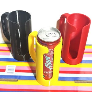 May include: Three 3D-printed can holders in black, yellow, and red. The yellow holder contains a can of Alani Energy drink. Each holder has a handle for easy carrying. The can holders are designed to keep beverages cold.