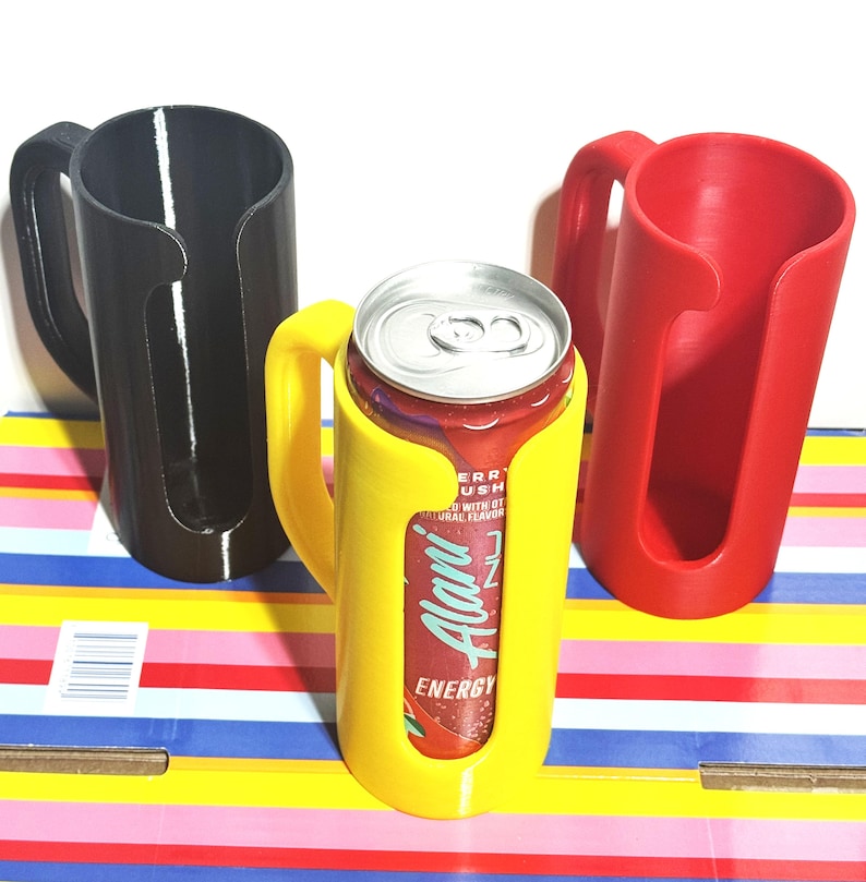 May include: Three 3D-printed can holders in black, yellow, and red. The yellow holder contains a can of Alani Energy drink. Each holder has a handle for easy carrying. The can holders are designed to keep beverages cold.