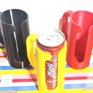May include: Three 3D-printed can holders in black, yellow, and red. The yellow holder contains a red and silver can with the text "Alani Energy". Each holder has a handle for easy carrying. The holders are designed to keep cans secure.