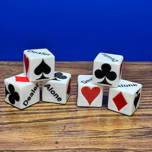 May include: Six white dice with black text and red and black suit symbols. The dice have the words "Dealer" and "Alone" printed on them. The suits include hearts, spades, clubs, and diamonds.