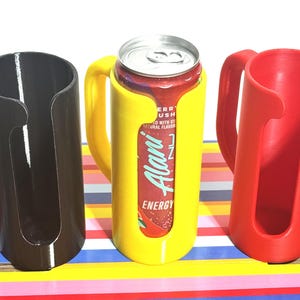 May include: Three 3D-printed can holders in black, yellow, and red. The yellow holder contains a can of Alani Energy drink. Each holder has a handle for easy carrying. The holders are designed to keep cans secure and insulated.