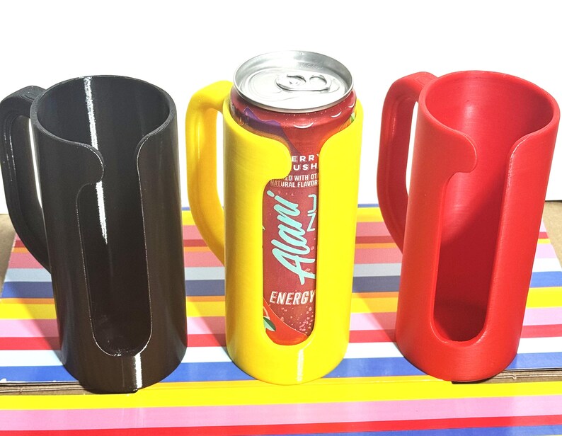 May include: Three 3D-printed can holders in black, yellow, and red. The yellow holder contains a can of Alani Energy drink. Each holder has a handle for easy carrying. The holders are designed to keep cans secure and insulated.