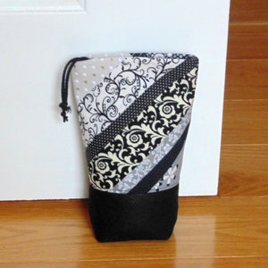 May include: A black and white patterned doorstop with a black fabric bottom. The doorstop is made of fabric and has a drawstring closure.