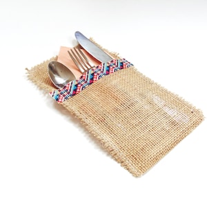 May include: A burlap cutlery holder with a colorful patterned trim. The holder contains a fork, knife, and spoon.