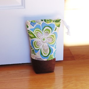 May include: A floral patterned doorstop with a brown bottom. The doorstop is made of fabric and has a white drawstring.