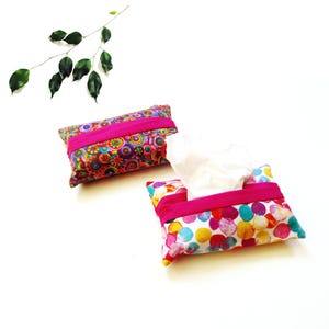 May include: Two rectangular fabric tissue holders with a center opening. One holder features a vibrant multicolored circular pattern, while the other displays a white background with colorful watercolor-style dots. Both have bright pink fabric bands.