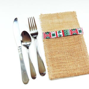 May include: A set of silverware, including a fork, knife, and spoon, is wrapped in a brown burlap napkin with a red, green, and white patterned ribbon.