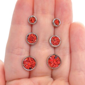 May include: A set of six red and silver stud earrings. The earrings are arranged in pairs, with the smallest pair on the left and the largest pair on the right.
