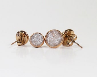 May include: A pair of gold stud earrings with white, sparkly, round insets.