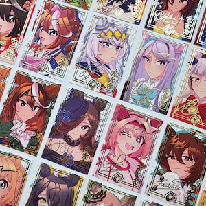 May include: A collection of anime-style trading cards featuring colorful illustrations of female characters. Each card has a gold border and showcases a different character with unique hairstyles and outfits. The cards are arranged in a grid pattern.
