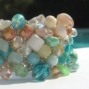 May include: A close-up of a beaded bracelet with a mix of turquoise, white, and pink beads. The bracelet is made with a silver wire and has a delicate, feminine look.