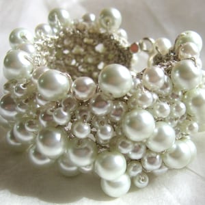 May include: A white pearl bracelet with a crocheted design. The bracelet is made of many small pearls and is a delicate and feminine piece of jewelry.