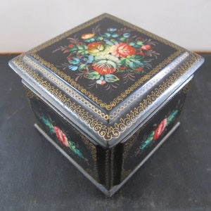 May include: A small black square box with a gold trim and floral design painted on the top. The flowers are red, pink, blue, and yellow.