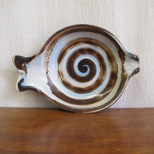 May include: A white ceramic dish with a brown and blue swirl design. The dish is shaped like a fish and has a handle on one side.