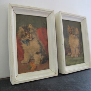 May include: Two framed pictures of kittens. The picture on the left shows a kitten with a blue ribbon around its neck. The picture on the right shows a kitten sitting on a green surface.