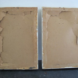 May include: Two white picture frames with brown cardboard backing. The cardboard is slightly torn and worn.