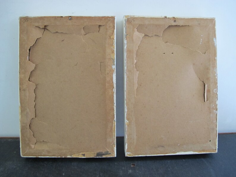 May include: Two white picture frames with brown cardboard backing. The cardboard is slightly torn and worn.