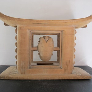 May include: A wooden stool with a carved design on the front. The stool has a rectangular base and a curved top.