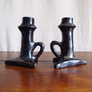 May include: Two black ceramic candle holders with a handle on the side. The holders have a simple, elegant design.