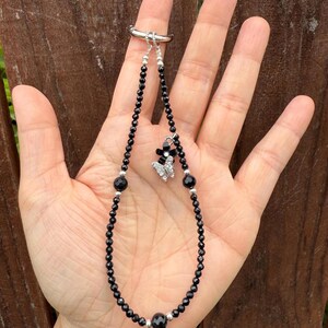 Puede incluir: Una pulsera de cuentas negras con un enganche de anillo plateado. La pulsera presenta un dije de mariposa con detalles en negro y plata. Las cuentas son peque&ntilde;as y redondas, con cuentas negras m&aacute;s grandes intercaladas. La pulsera se sujeta con un anillo plateado.