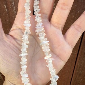 Puede incluir: Un collar con peque&ntilde;as piedras irregulares de cuarzo transparente. El collar tiene un cierre dorado y una cuenta de cuarzo transparente m&aacute;s grande y redonda en el centro. Las piedras son de color claro y parecen pulidas.