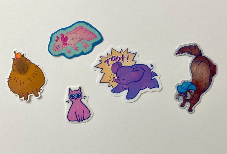 May include: A set of five colorful stickers featuring various animals. The stickers include a pink axolotl, a brown capybara, a purple elephant with the word "Toot!" in a yellow speech bubble, a pink cat, and a brown ferret wearing a blue hat.