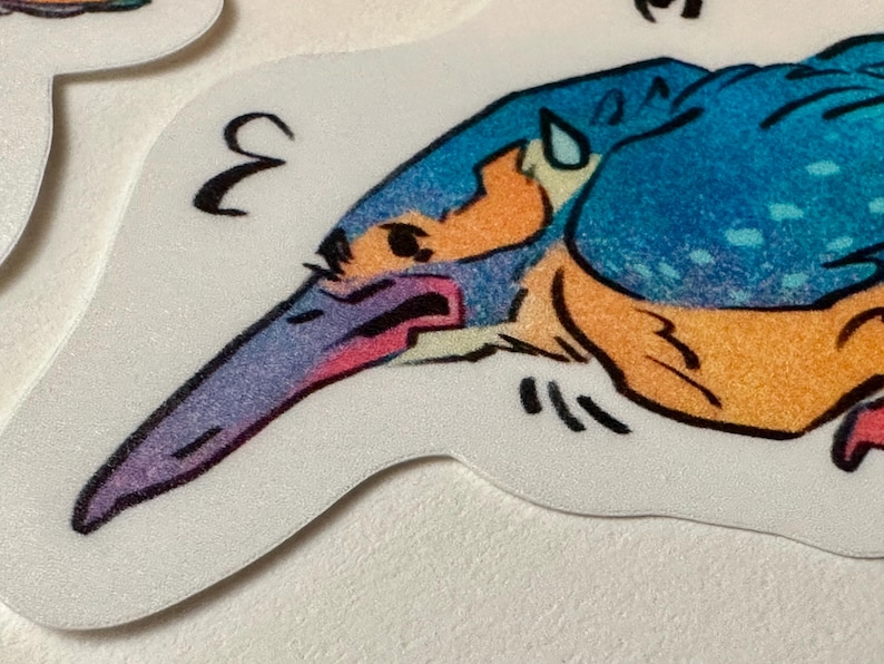 Peut inclure: Un autocollant repr&eacute;sentant une illustration stylis&eacute;e d'un martin-p&ecirc;cheur. L'oiseau est de couleur bleue, orange et violette avec des d&eacute;tails noirs. Le chiffre "3" est imprim&eacute; en noir sur l'autocollant.