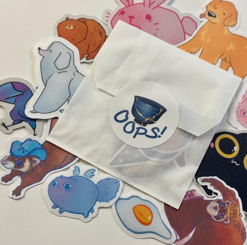 May include: A white envelope with a sticker that says "Oops!" and a variety of colorful stickers featuring animals, food, and other designs.