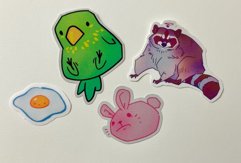 May include: Four colorful stickers featuring a green parrot, a pink bunny, a blue and white egg, and a purple raccoon.