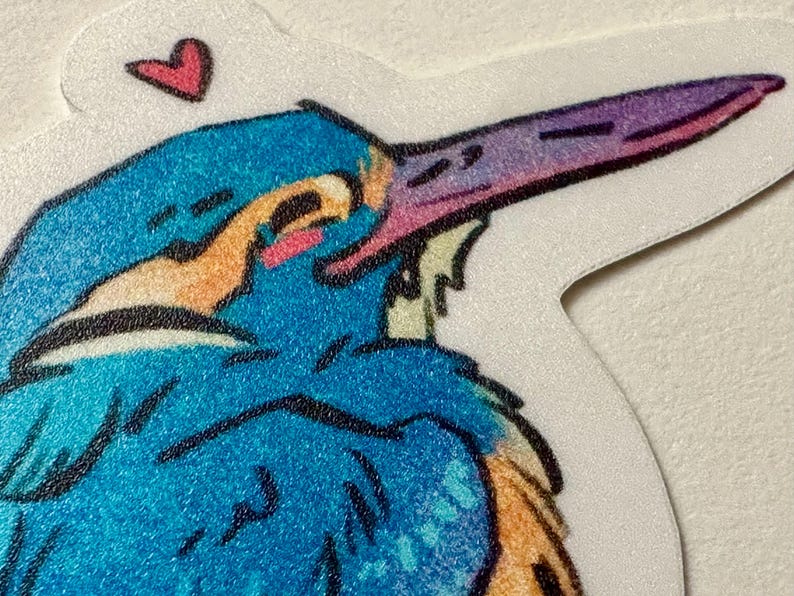Peut inclure: Un autocollant repr&eacute;sentant une illustration color&eacute;e d'un oiseau au long bec. L'oiseau a des teintes bleues, oranges et violettes, avec un petit c&oelig;ur rose au-dessus de sa t&ecirc;te. L'autocollant a une bordure blanche.