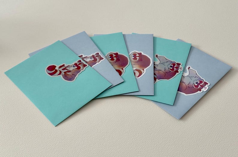 May include: Six light blue cards with colorful cartoon raccoon stickers on them. The stickers feature a raccoon with a red and white striped tail.