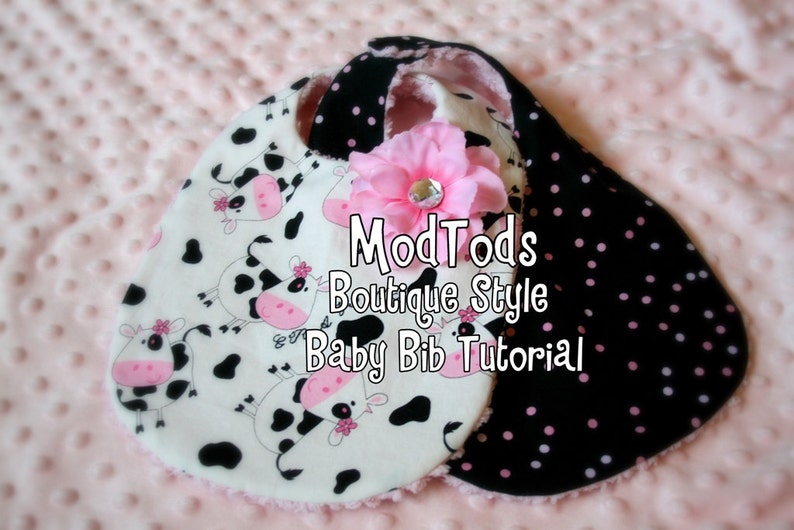 May include: Two baby bibs with a pink flower and text. One bib features a cow print on white fabric, the other has black fabric with pink polka dots. The text reads "ModTods Boutique Style Baby Bib Tutorial."