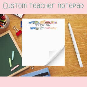 May include: A custom teacher notepad with the text "Custom teacher notepad" at the top. The notepad has a watercolor design of school supplies and the name "Mrs. Kirkland". The notepad is on a wooden desk with school supplies.