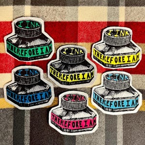 May include: Six ink bottle stickers with the text "I Ink Therefore I Am" in various colors. The ink bottles are black with a silver cap and a colored banner across the bottom. The background is a red and brown plaid.