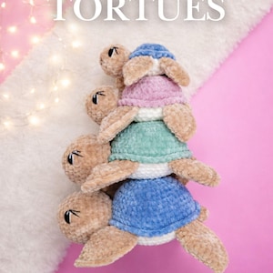 Peut inclure: Une pile de tortues crochetées bleues, vertes et roses, avec le texte "PATTERNS TORTUES" et "Luna Olivia Crochet". Les tortues ont un aspect doux et texturé. Le fond est rose et blanc, avec des guirlandes lumineuses.
