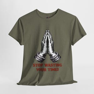 May include: A green t-shirt with a black and white illustration of praying hands. The text "STOP WASTING YOUR TIME!" is printed in red below the illustration.