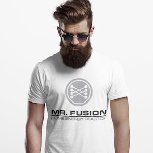 May include: White t-shirt featuring a grey circular graphic and the text "MR. FUSION HOME ENERGY REACTOR" in black. The graphic shows interconnected circles. The shirt is worn by a person with a beard and sunglasses.