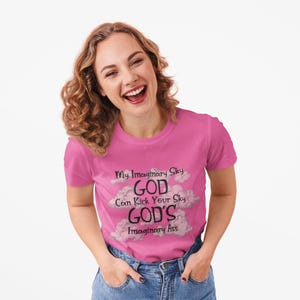 May include: A pink t-shirt with the text "My Imaginary Sky GOD Can Kick Your Sky GOD'S Imaginary Ass" in black and white, with cloud graphics. The shirt is being worn by a person.