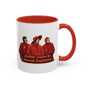 May include: White ceramic mug with a red interior and handle. The mug features a graphic of three figures in red robes with the text "Nobody expects the Spanish Inquisition!"