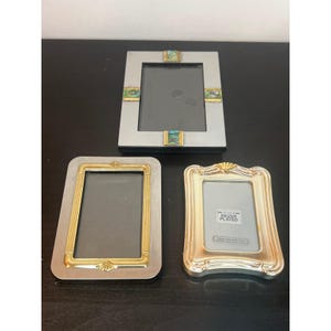 May include: Three rectangular picture frames. The top frame is silver-toned with four inlaid abalone shell accents. The bottom left frame has a brushed silver border with a gold-toned inner trim. The bottom right frame is silver-plated with a scalloped edge.