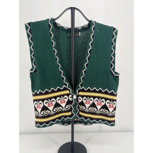 May include: A dark green knit vest featuring a V-neckline and a single button closure. The garment displays a decorative band with white heart-shaped motifs, red accents, and yellow horizontal stripes along the lower front section.
