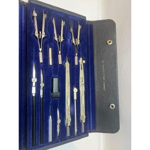May include: A vintage drafting set in a black leather case with a blue velvet interior. The set includes various compasses, dividers, and other drawing tools. The case is marked "Keuffel & Esser Co."