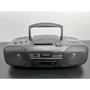 May include: A black Sony portable CD and cassette player boombox featuring a top-loading CD compartment, a central carrying handle, dual front-facing speakers with metal grilles, and various control buttons for playback and track selection.