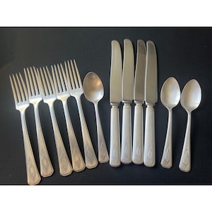 May include: A set of silver-toned flatware consisting of five forks, four knives, and three spoons. Each piece features a slender handle with a decorative etched diamond-shaped motif near the base, showcasing a consistent metallic finish throughout.