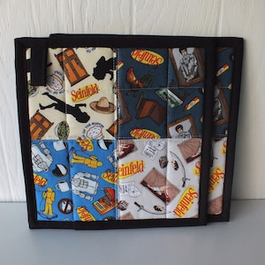 May include: Two square quilted pot holders with a black border. Each pot holder is made of fabric squares with images and text from the TV show Seinfeld. The pot holders are on a white surface.