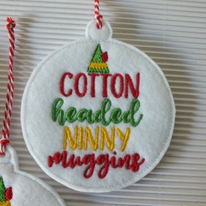 May include: White felt Christmas ornament with red and green embroidery that reads "Cotton headed ninny muggins". A green elf hat with a red bow is embroidered at the top of the ornament.