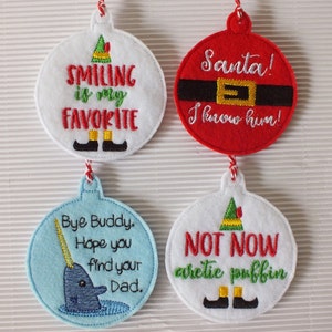 May include: Four felt Christmas ornaments with embroidered designs. The first ornament is white with green and black embroidery that says "Smiling is my favorite". The second ornament is red with black and gold embroidery that says "Santa! I know him!". The third ornament is light blue with blue and yellow embroidery that says "Bye Buddy. Hope you find your Dad." The fourth ornament is white with green, black, and yellow embroidery that says "Not Now arctic puffin".