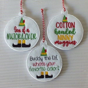 May include: Three round felt ornaments with embroidered elf designs and text. The first ornament says "Son of a Nutcracker". The second ornament says "Cotton headed Ninny Muggins". The third ornament says "Buddy the Elf, what's your favorite color?"